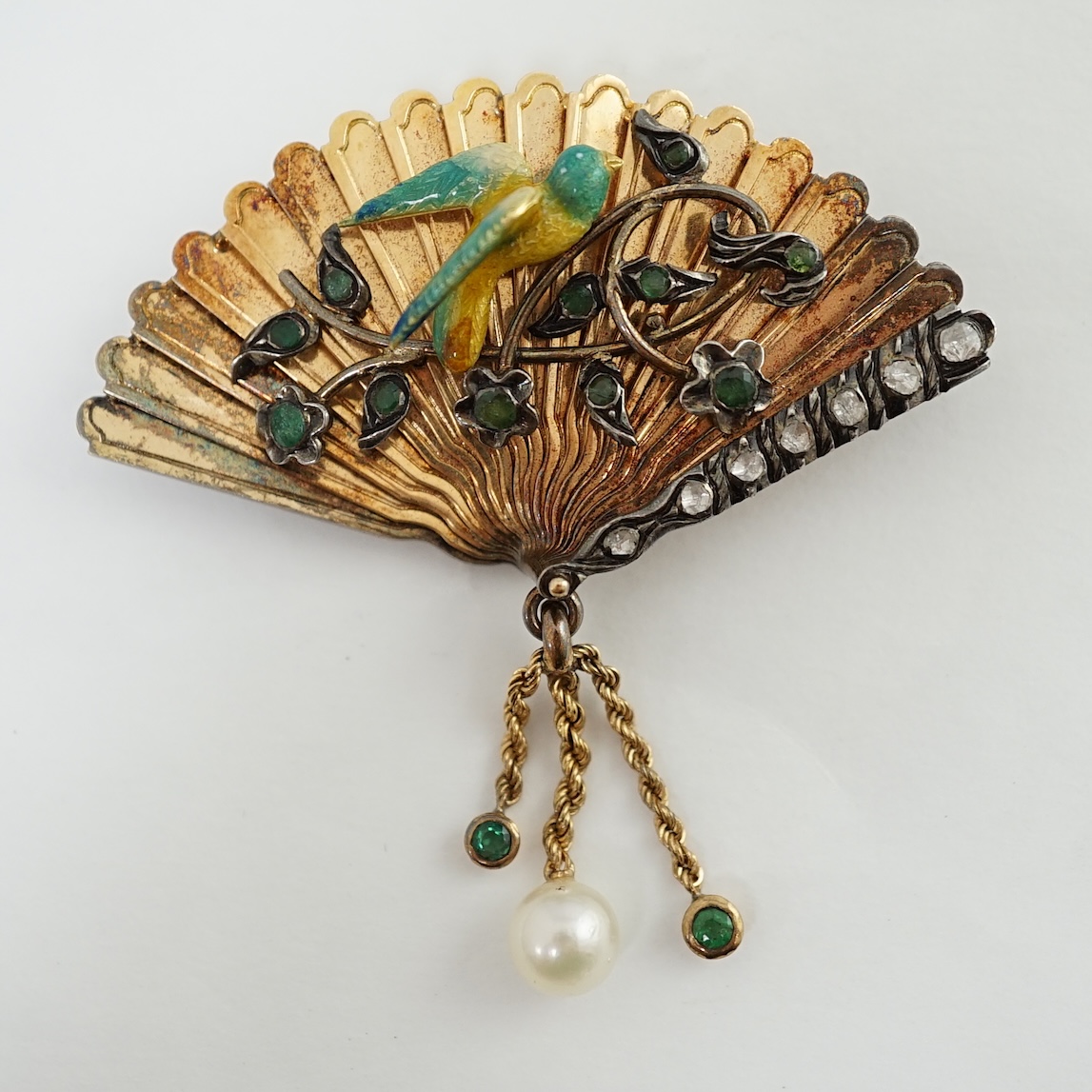 A gold (test as 15ct), emerald, rose cut diamond and enamel set brooch, modelled as a fan with applied parrot on a branch